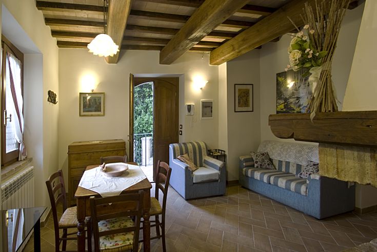Soggiorno luminoso con cucina a vista, legno a vista e dettagli rustici, situato in un casale storico in Umbria.