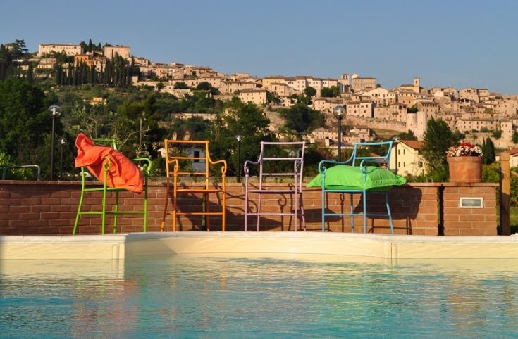 Bunte Liegen am Pool mit Blick auf ein historisches Dorf in Umbrien.