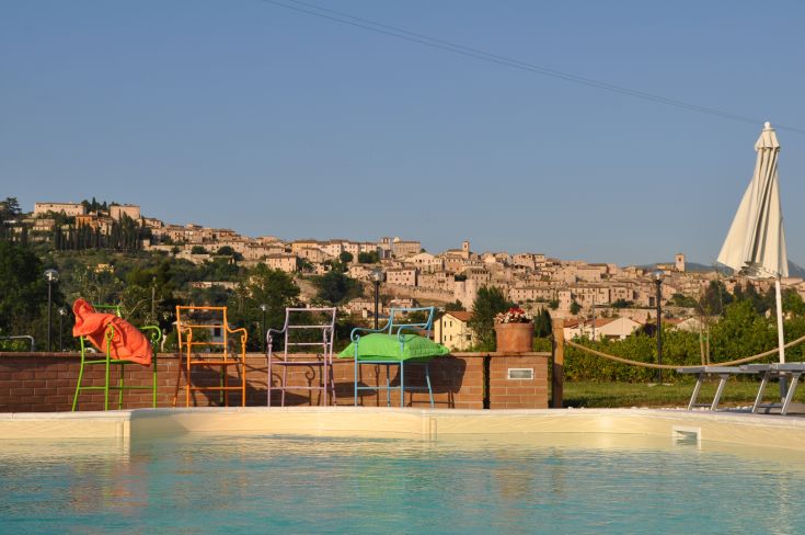 Poolbereich mit bunten Stühlen und Blick auf ein charismatisches umbrisches Dorf.