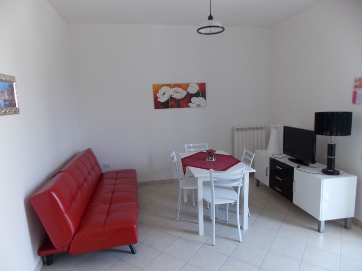 Gemütliches Interieur mit rotem Sofa und Essbereich, beleuchtet von natürlichem Licht.