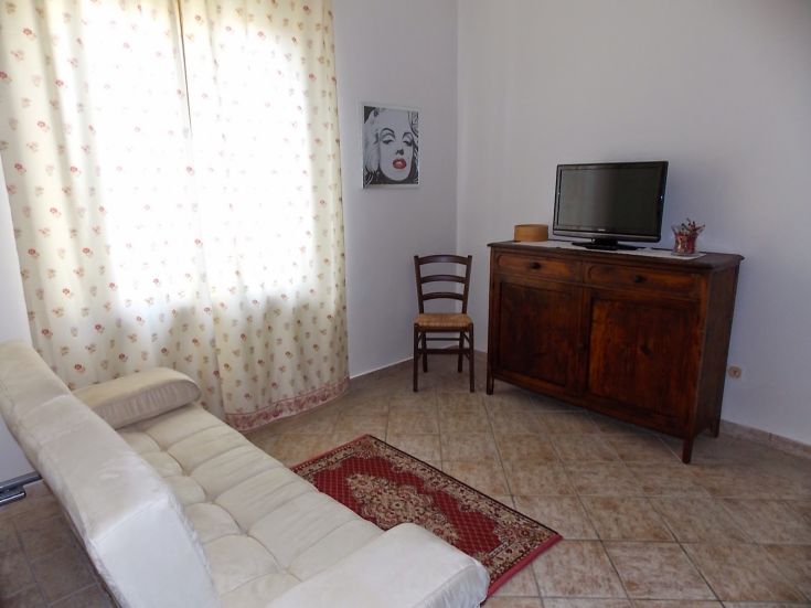 Helles Wohnzimmer mit schlichter Einrichtung, bestehend aus einem Sofa und einem Fernseher.