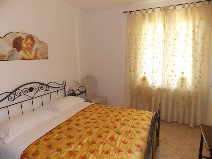 Einfaches Zimmer mit einem Doppelbett, schlichten Dekorationen und leichten Vorhängen.