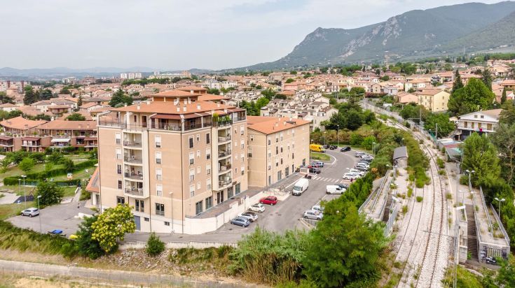 Struttura residenziale moderna con camere e appartamenti, circondata da verde e con panorama su colline.
