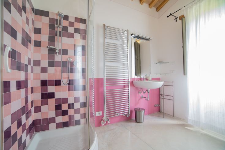 Einfaches Badezimmer mit pastellfarbenen Fliesen, Dusche und funktionalen Accessoires.