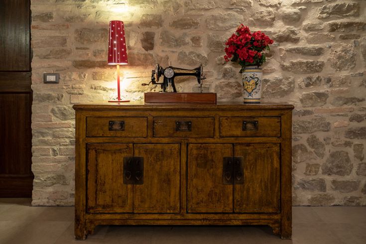 Eine Holzkommode mit einer Nähmaschine und einer Vase mit roten Blumen schmückt dieses Zimmer im Vintage-Stil.