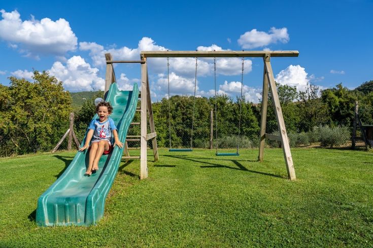 Ein Kind lächelt, während es von einer kleinen Rutsche in einem gut gepflegten grünen Garten rutscht.
