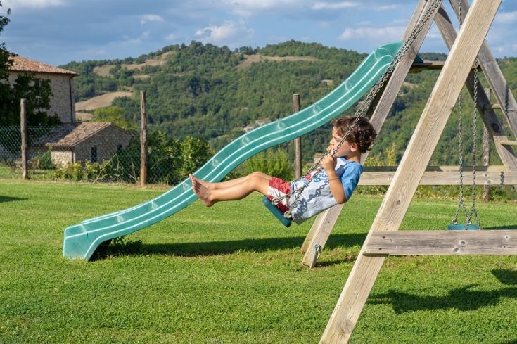 Ein Kind spielt freudig auf einer Schaukel in einem geräumigen grünen Garten, umgeben von Bäumen.