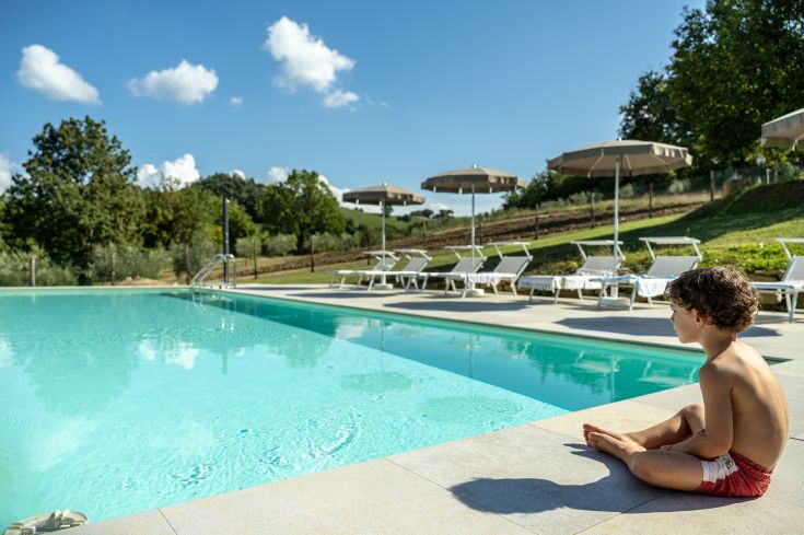 Ein Kind schaut auf einen Pool, der von Schirmen und einer ruhigen Landschaft in der Natur umgeben ist.