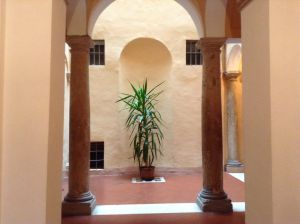 Una corte interna di un palazzo, caratterizzata da piante verdi e colonne antiche.