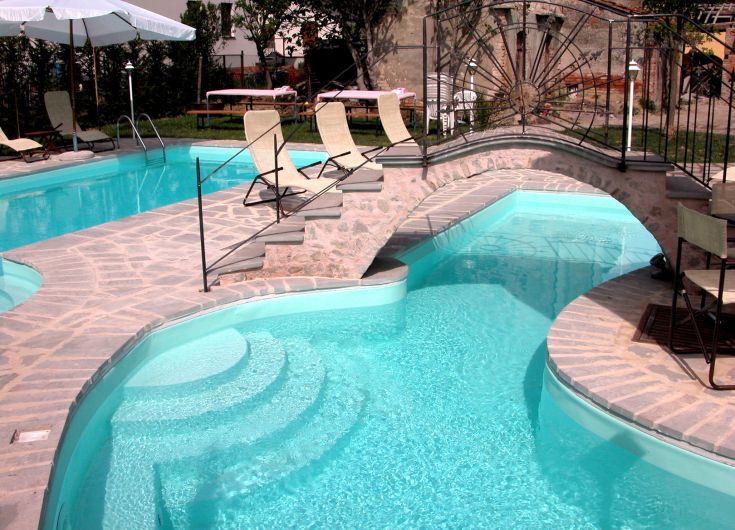 Une piscine d'été entourée d'un jardin et d'espaces de détente, comprenant un petit pont.