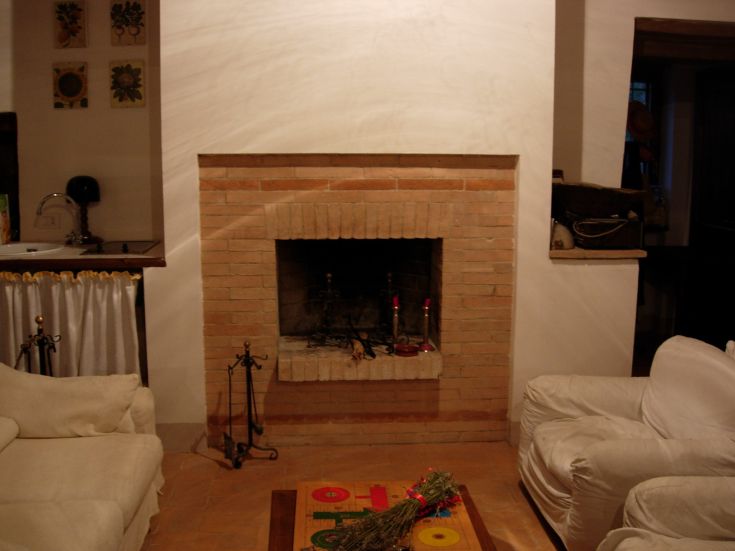 Ein gemütliches Wohnzimmer mit einem Kamin aus Ziegelsteinen, ausgestattet mit weißen Sofas und rustikalen Details.