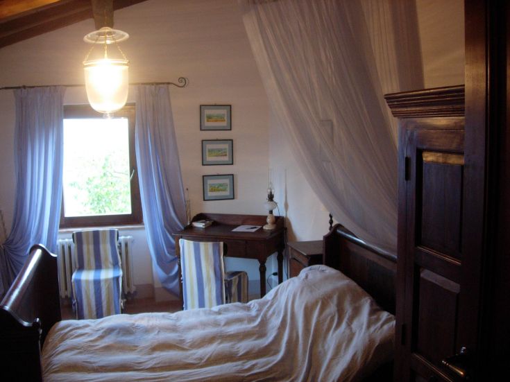 Ein einfacher Raum mit Fenstern, die Licht hereinlassen, Holzmöbeln und leichten Vorhängen.