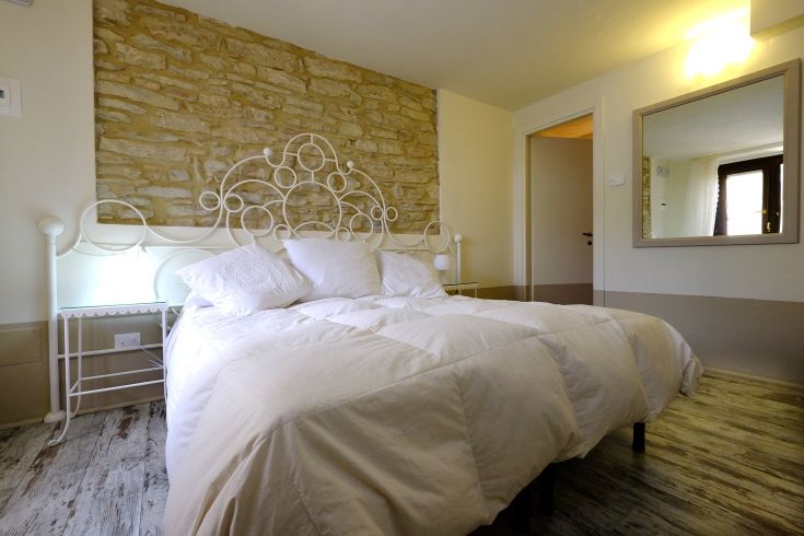 Ein einfaches Zimmer mit einem Doppelbett und Steinenwänden. Warmes Licht trägt zur entspannenden Atmosphäre bei.