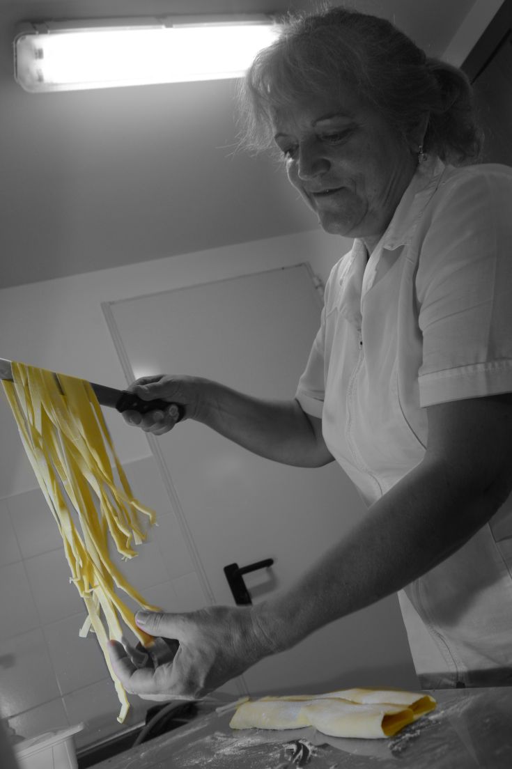 Eine erfahrene Köchin zeigt frisch zubereitete Pasta, die die lokale Kochtradition repräsentiert.