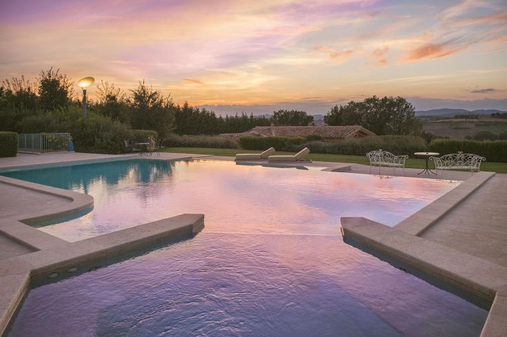 An infinity pool reflects the hues of the sunset, surrounded by lush greenery.