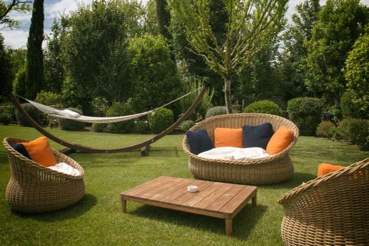 A serene outdoor space with wicker sofas and a wooden table surrounded by plants and shrubs.