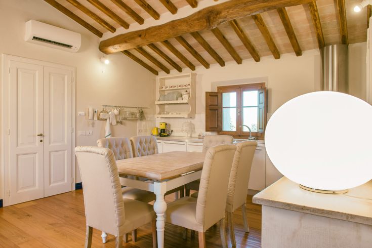 Bright kitchen with a wooden table and upholstered chairs, illuminated by a simple lamp.