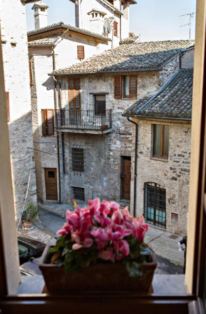 Un angolo tranquillo del centro storico di Spello, caratterizzato da fiori colorati e architettura in pietra.