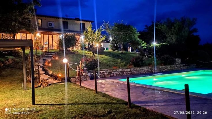 Una scena di un agriturismo con piscina, illuminato da una luce morbida del crepuscolo.