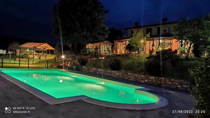 Serata serena in un agriturismo, con piscina illuminata e vista su un paesaggio verde.