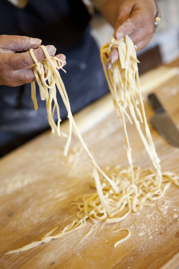 Un cuoco prepara la pasta fresca a mano, visibile tra le sue mani. Un gesto tipico e rappresentativo della cucina italiana.