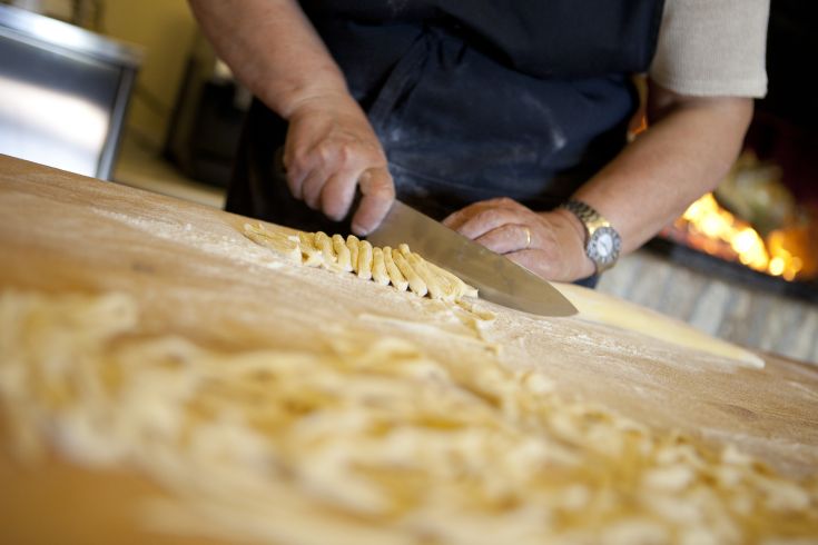 Un artigiano stende la pasta fresca su un tavolo di legno cosparso di farina.