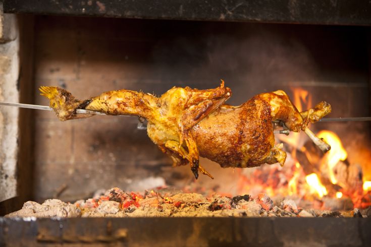 Un pollo arrosto su uno spiedo, cotto su un fuoco vivace, rappresenta un piatto della tradizione culinaria italiana.