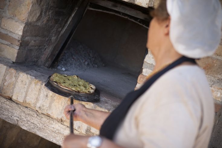 Una donna sta preparando una pizza in un forno a legna, tipica della cucina umbra.