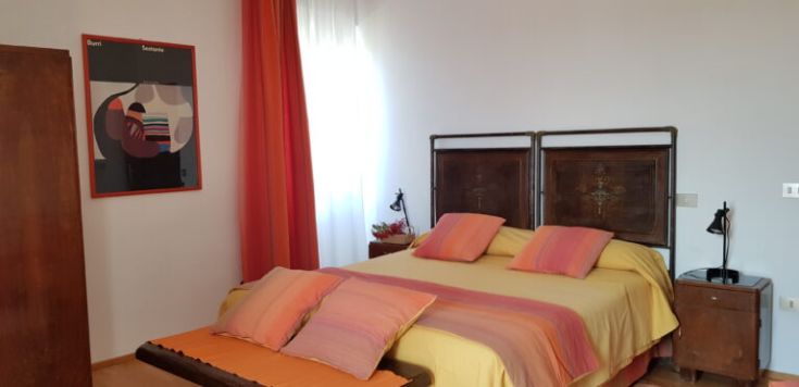 A bedroom with a double bed, simple furnishings, and natural light illuminating the space.