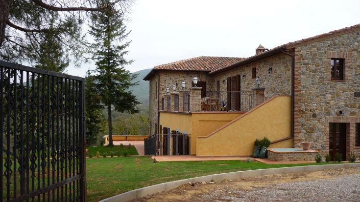 A renovated farmhouse surrounded by lush greenery, featuring independent apartments amidst vineyards and olive trees.