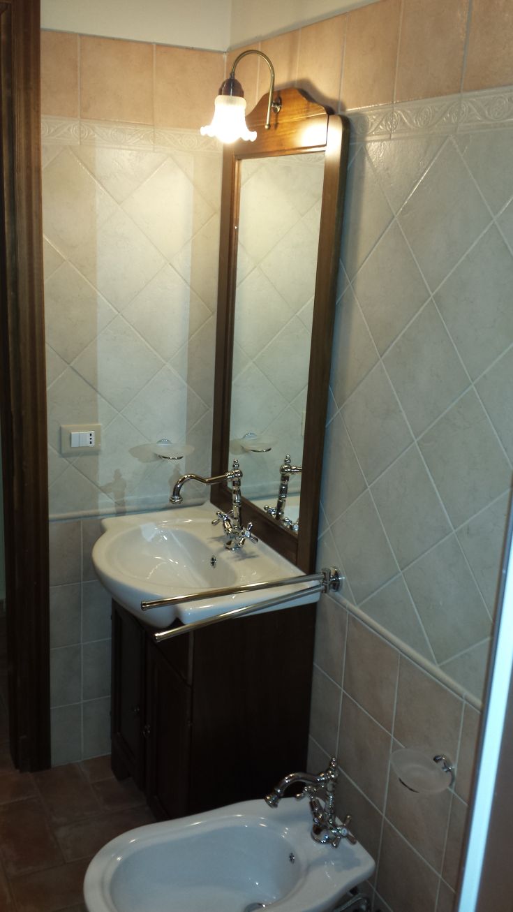 Simple bathroom featuring a sink and bidet, a framed mirror, soft lighting, and light-colored tiles.