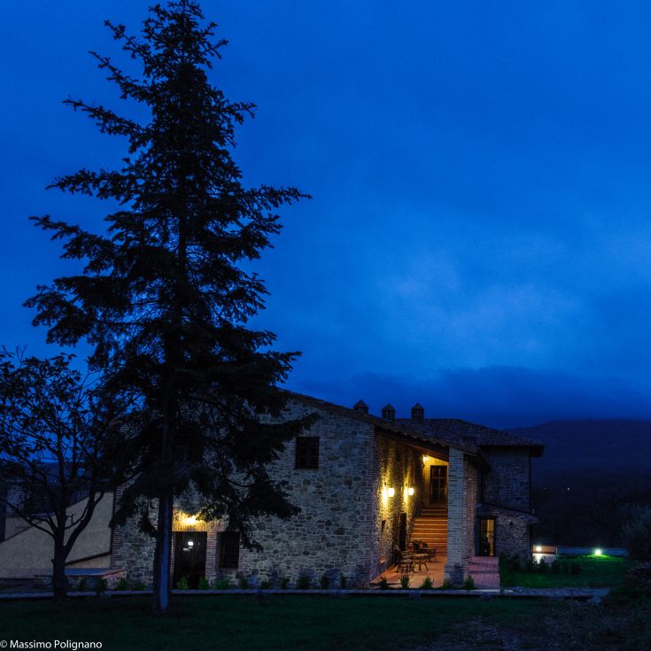The renovated farmhouse glows at sunset, surrounded by hills and nature.