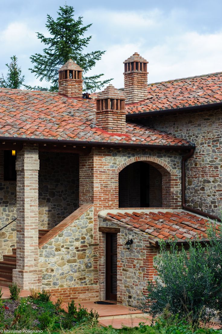 A stone farmhouse with a red roof and chimneys, surrounded by the Umbrian countryside.