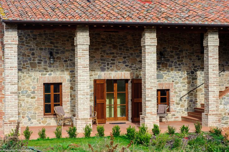 A restored farmhouse made of stone and bricks, featuring a porch and a well-kept garden in a natural setting.