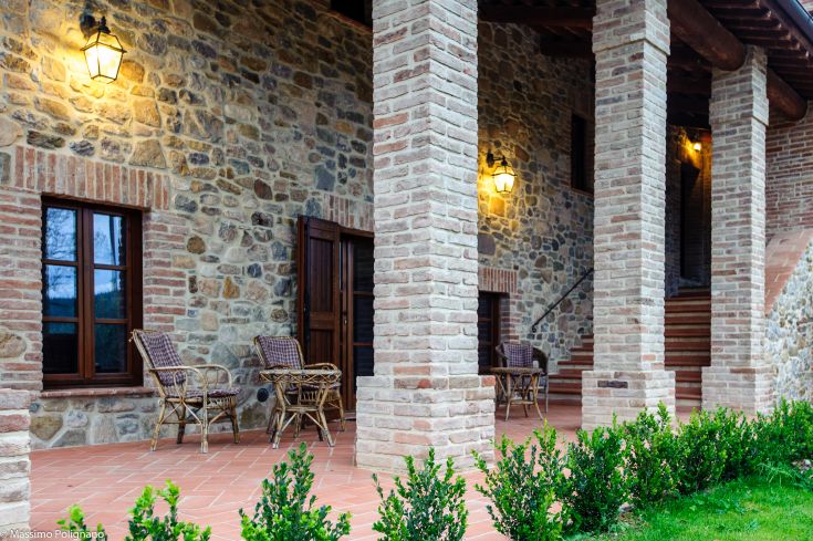 A charming farmhouse with stone columns, warm lighting, and outdoor seating areas.