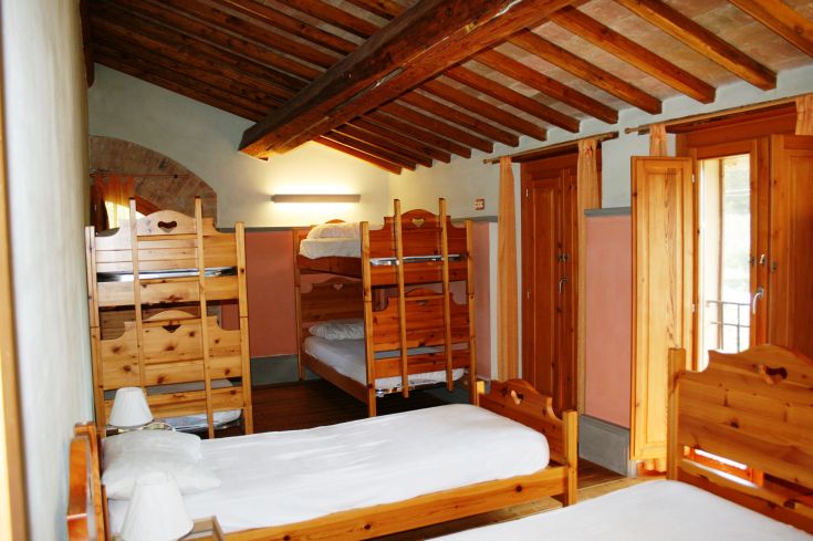 Simple room with wooden bunk beds, featuring brightly colored walls and overlooking a green environment.