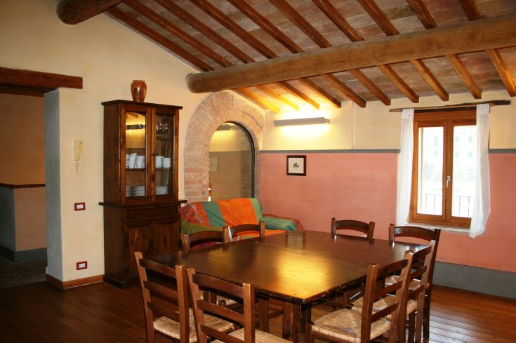 A cozy living room with a large wooden table, warm-toned furniture, and inviting lighting, perfect for socializing.