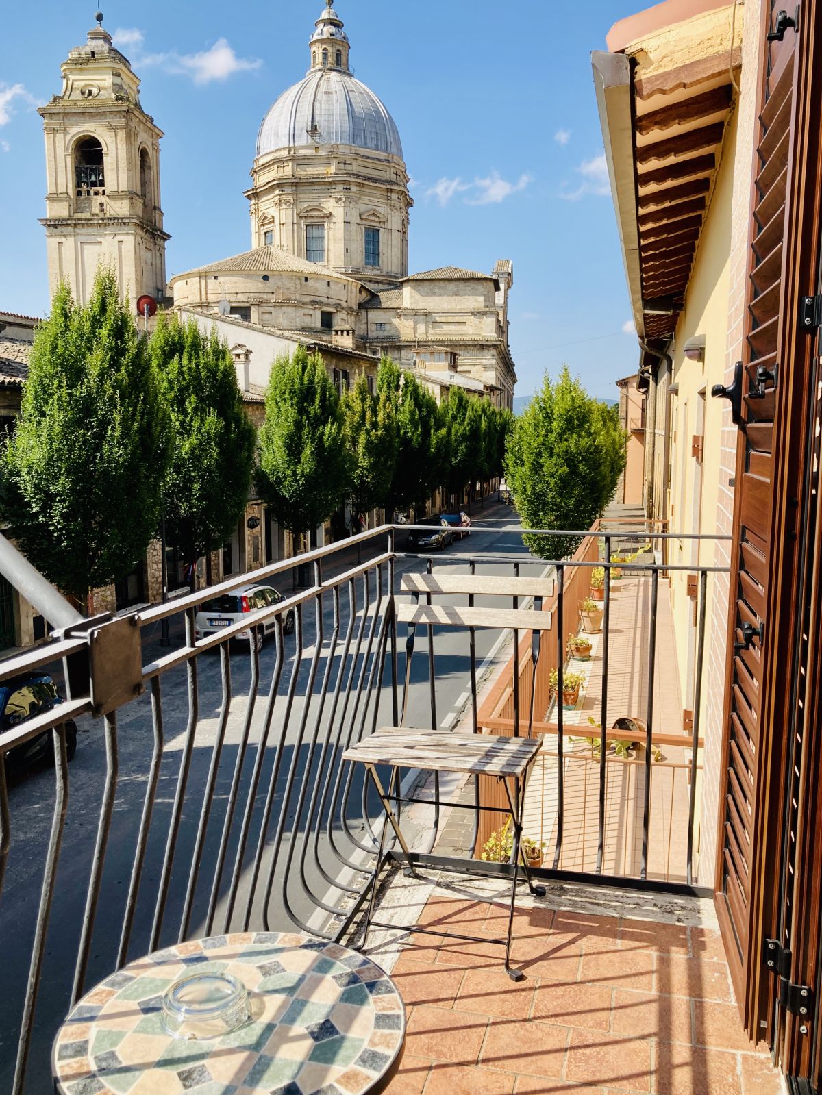 A balcony overlooking the historic architecture of an Umbrian town, surrounded by trees and a clear sky.