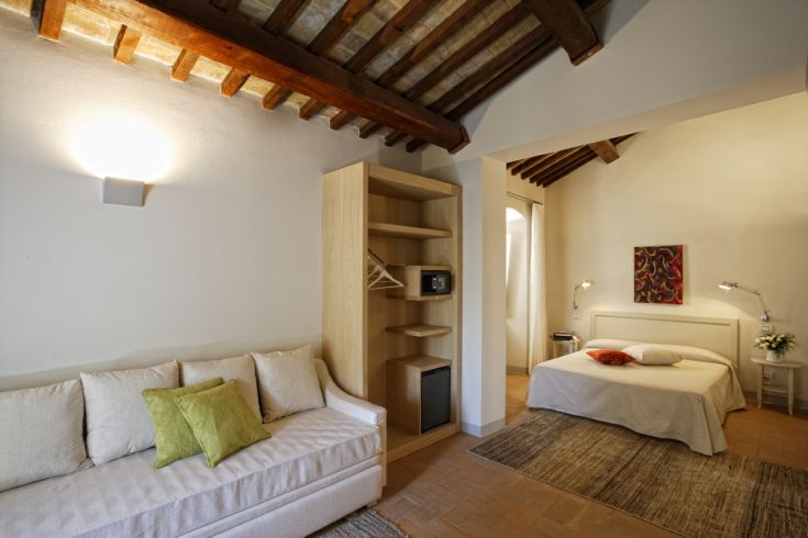 Interni di una camera d'hotel con letti e un divano, arredamenti semplici e confortevoli.