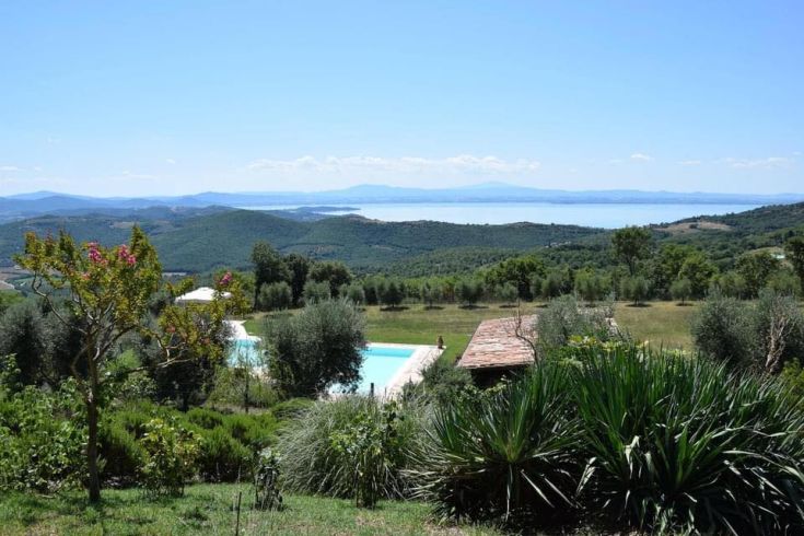 Scena tranquilla con piscina e colline verdi, con vista sul Lago Trasimeno.