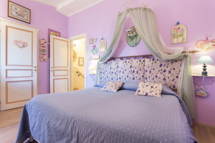 Camera da letto semplice in tonalità viola, con decorazioni floreali e un'atmosfera intima.