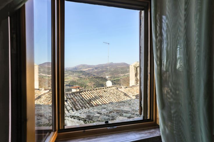 Panorama da una finestra che mostra colline verdi e tetti di terracotta.