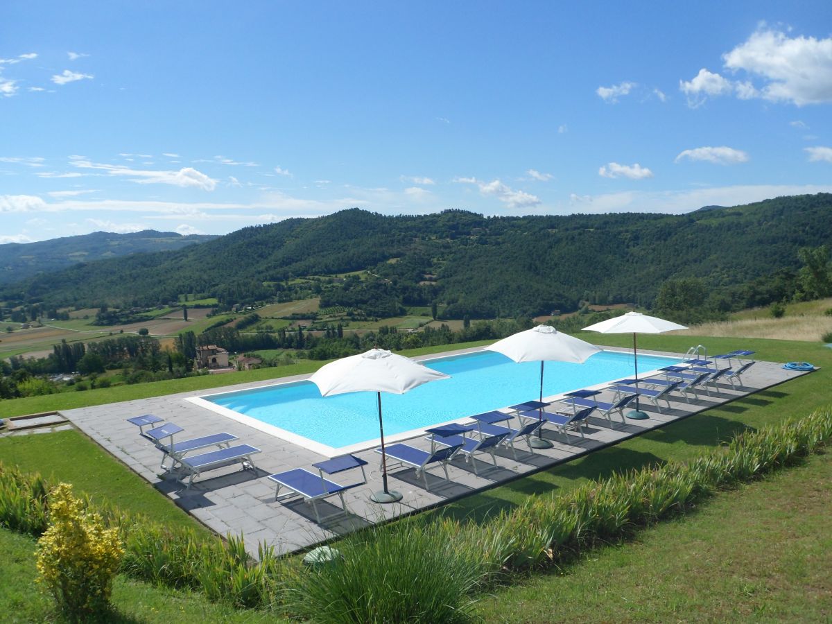 A swimming pool in the Umbrian countryside, surrounded by lush green hills.