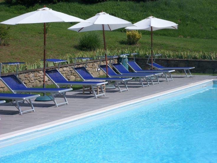 Moments de détente au bord de la piscine dans un agriturisme entouré par le vert de l'Ombrie, avec des parasols blancs et des chaises longues bleues.