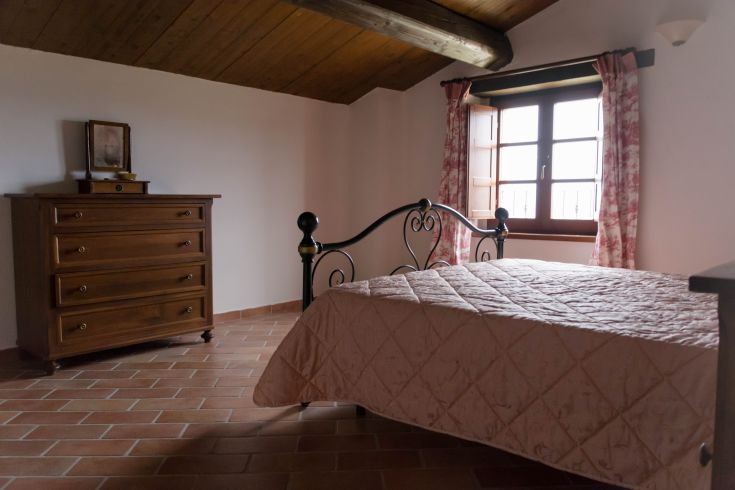 Intérieur d'un agriturismo en Ombrie avec un lit double et des décorations en bois qui captent la lumière naturelle.