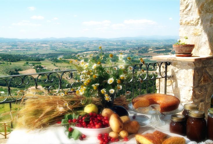 Ein Tisch, der mit Obst, Brot und Marmelade gedeckt ist, mit Blick auf eine ruhige umbrische Landschaft.