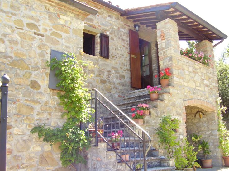 Edificio in pietra tra dolci colline, circondato da fiori e un ambiente tranquillo.