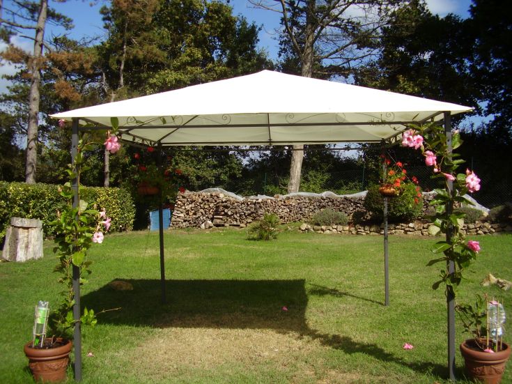 Gazebo bianco in un giardino, circondato da fiori e piante, perfetto per eventi all'aperto.