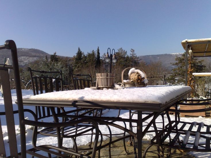 Spazio esterno con tavolo coperto di neve e panorama sulle colline in una giornata serena.