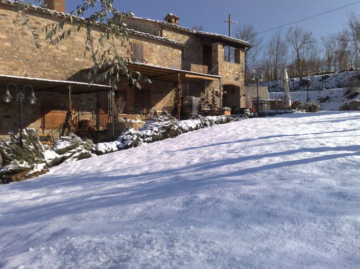 Palazzo in pietra coperto di neve, immerso in un paesaggio di colline e alberi.